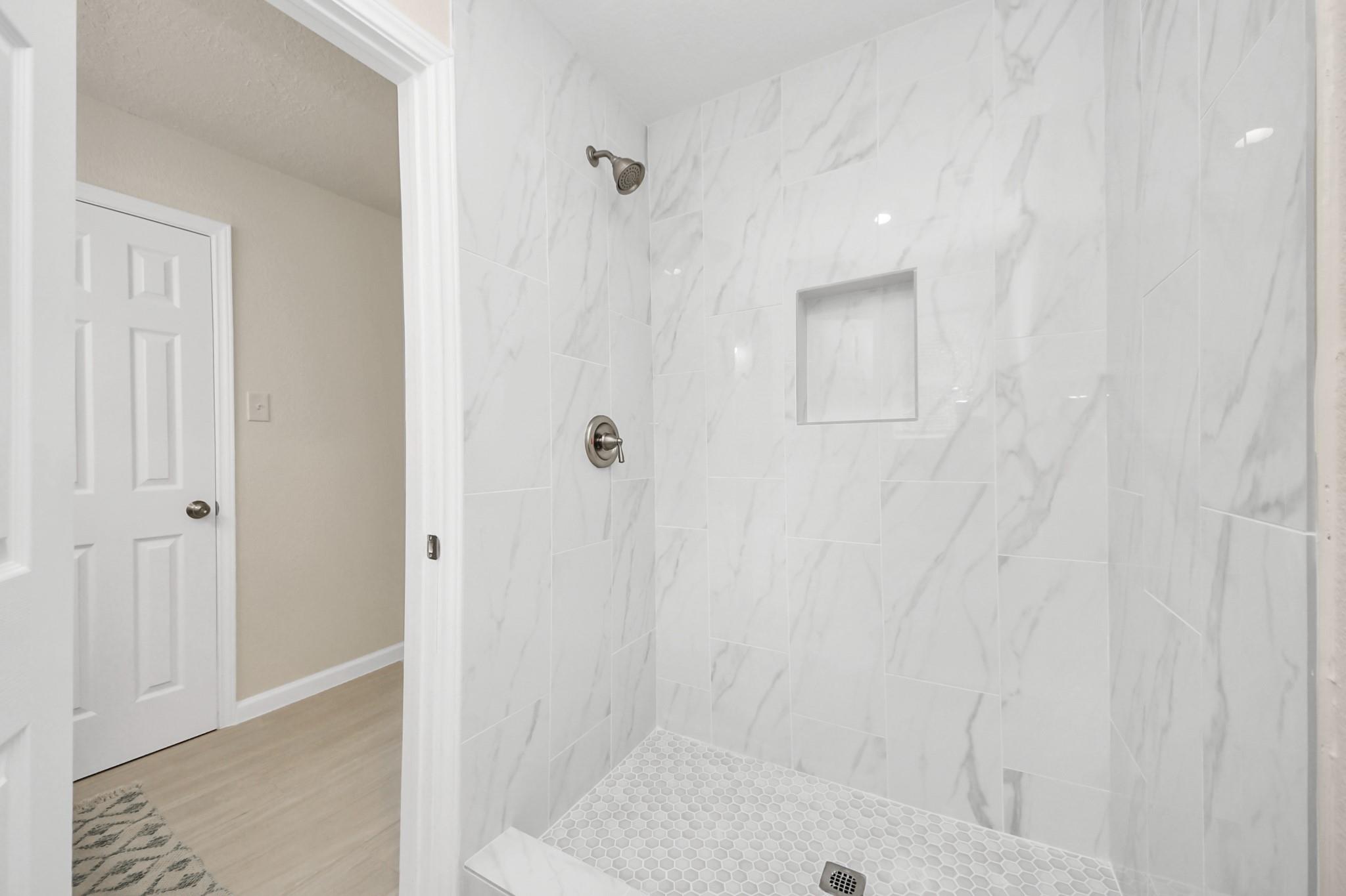 Bathroom shower with marble-look tile, a recessed niche, and a hexagonal mosaic floor.