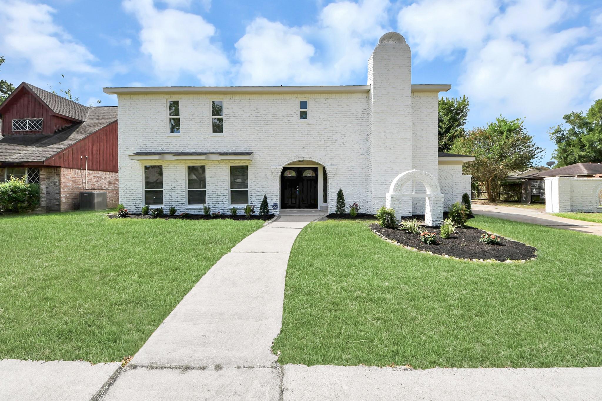 Two-story white brick house with a tall chimney, arched entrance, and curved front walkway.
