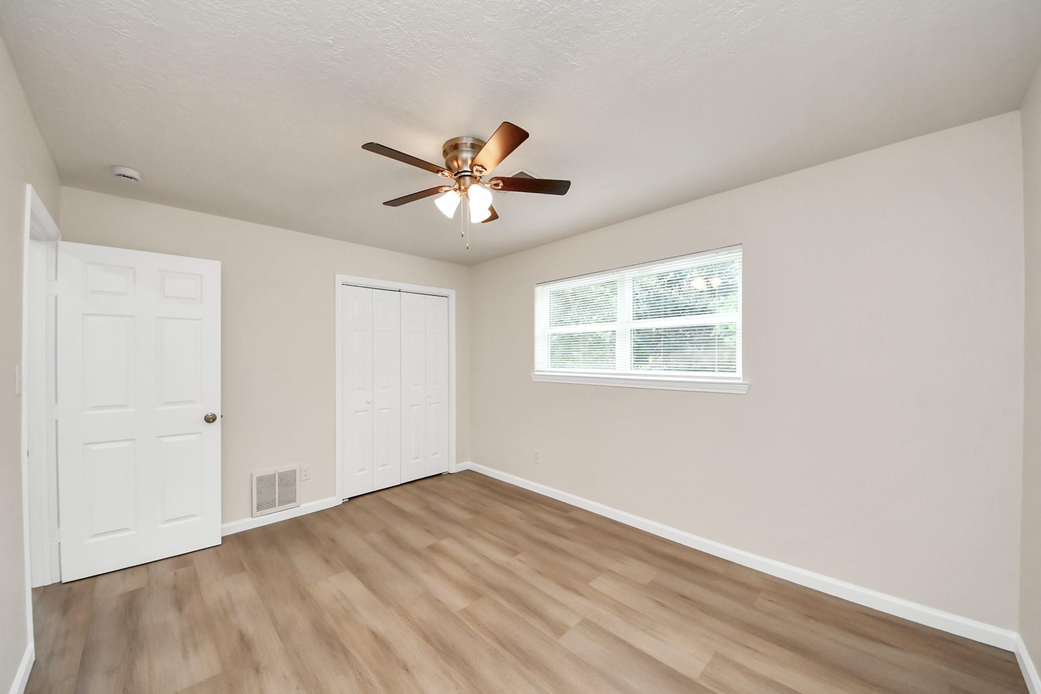 Empty bedroom with wood-look flooring, a window with blinds, and a ceiling fan.
