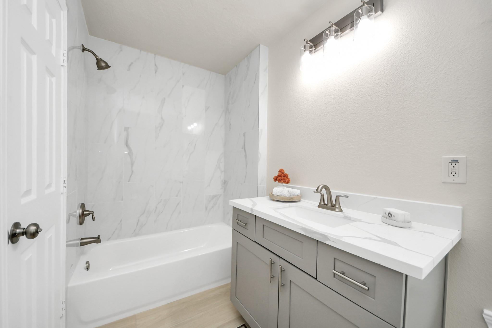 Bathroom with a marble-look tub surround and gray vanity with a white countertop.