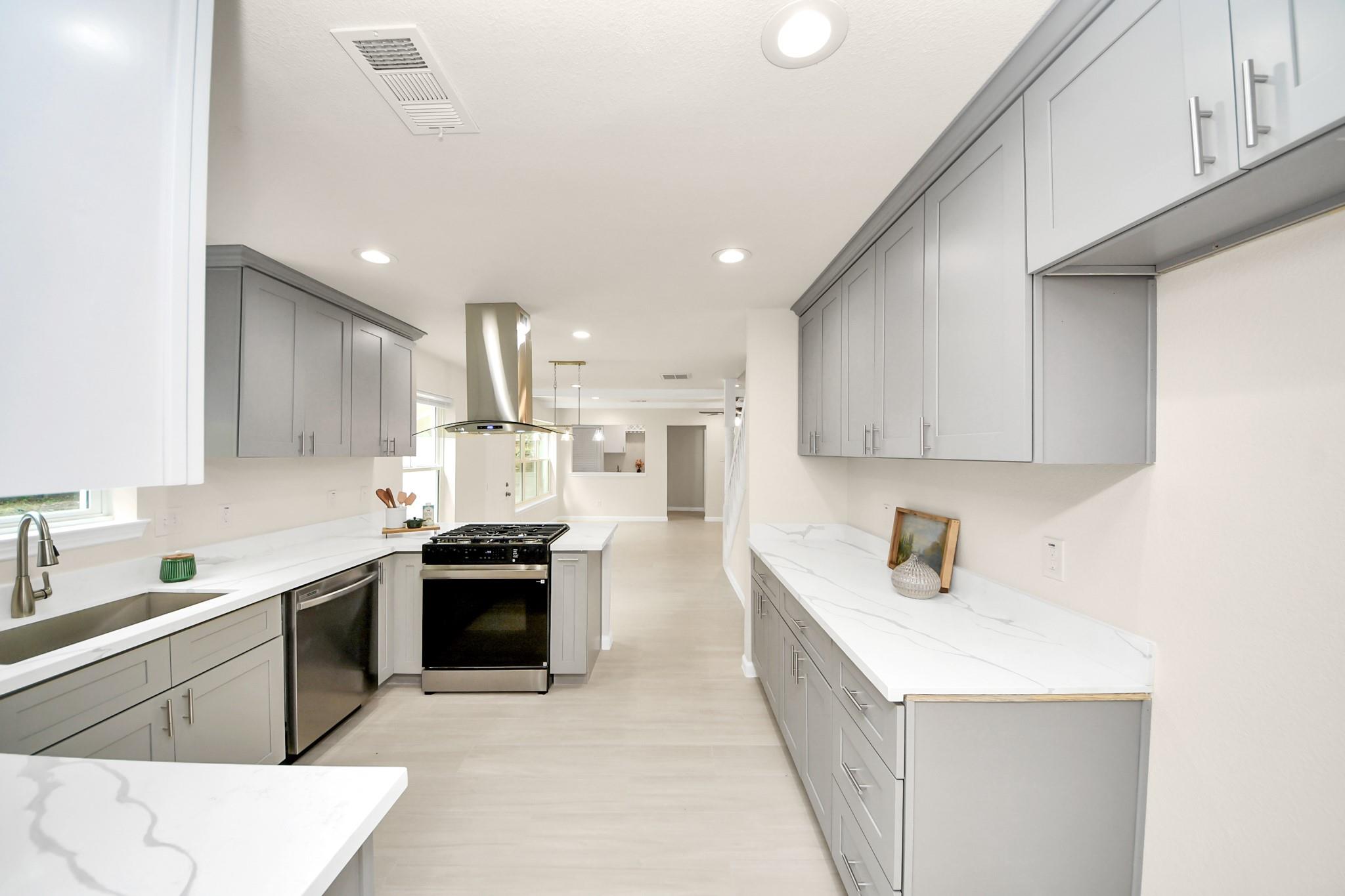 Kitchen with gray cabinets, white veined counters, and a stainless steel gas range.