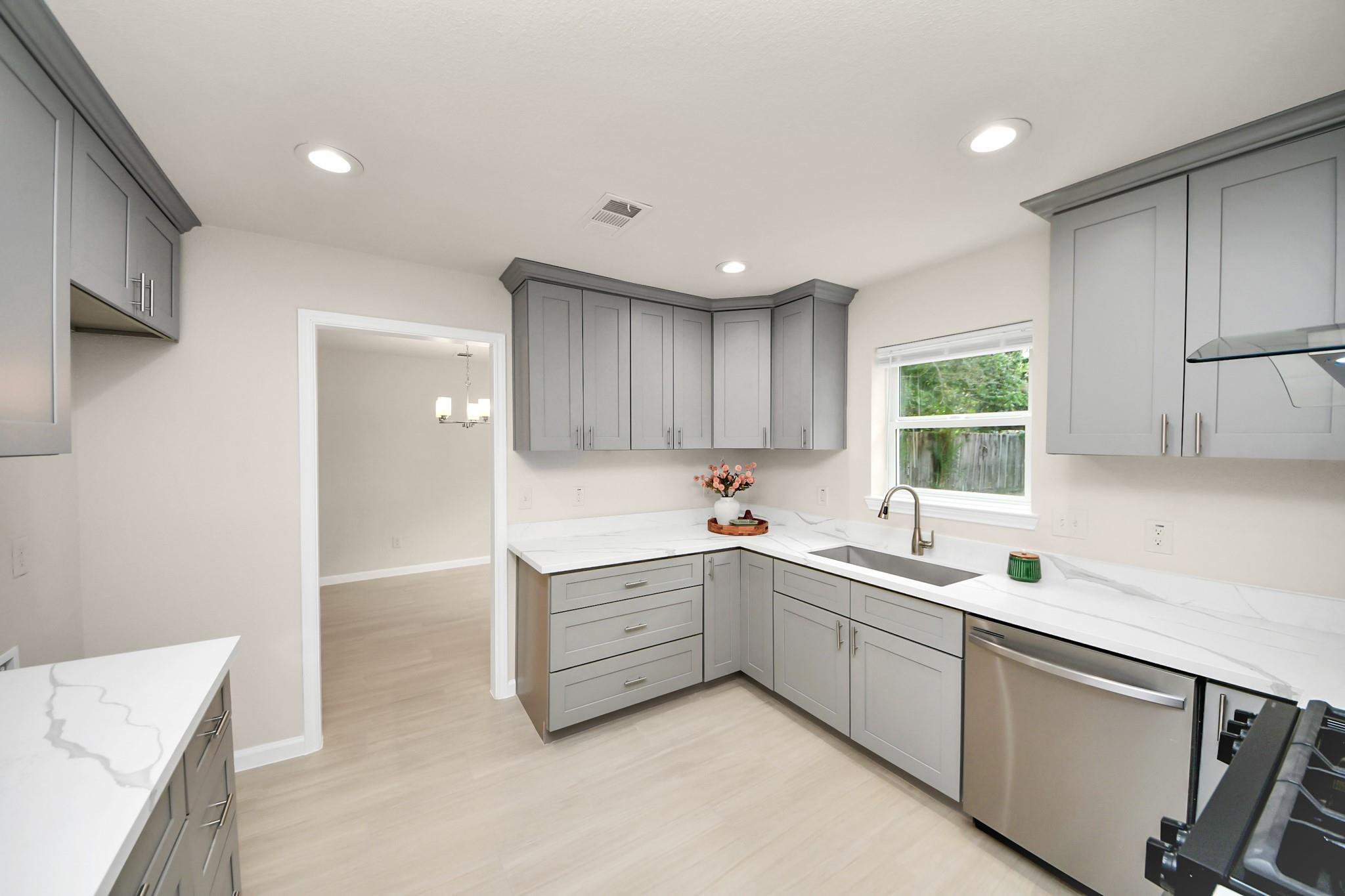 Kitchen with gray cabinets, white veined countertops, and a sink beneath the window.