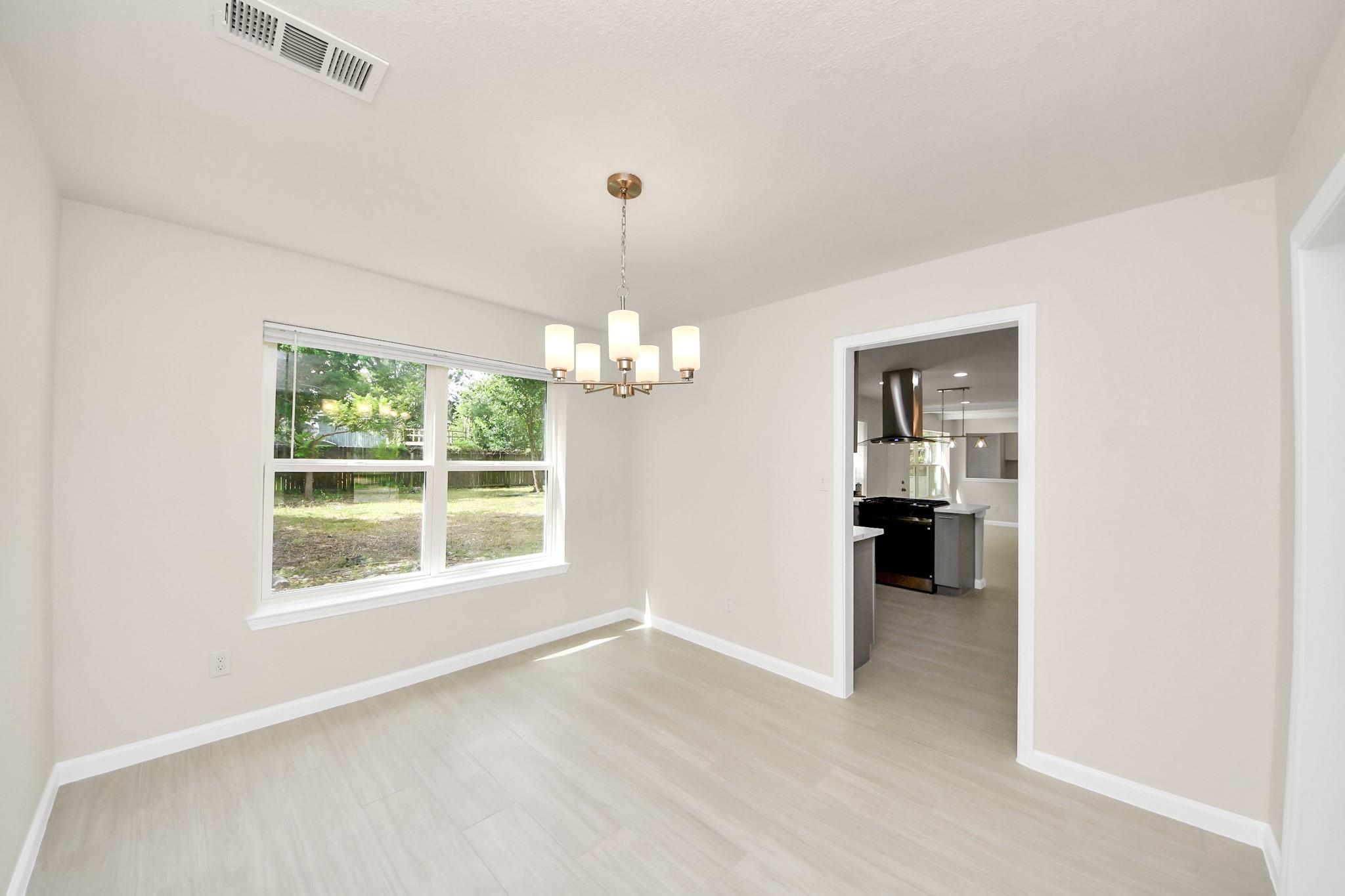 Vacant dining room with a chandelier, large backyard-facing window, and doorway to the kitchen.