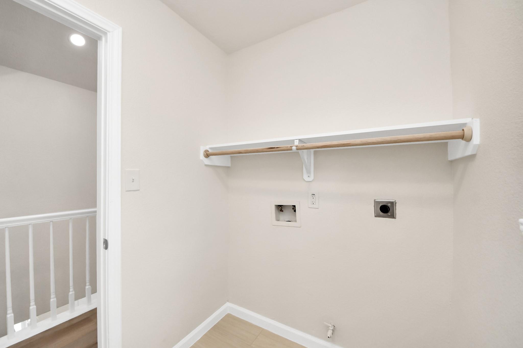 Laundry closet with a wooden hanging rod and washer hookups beside a doorway to a railed landing.