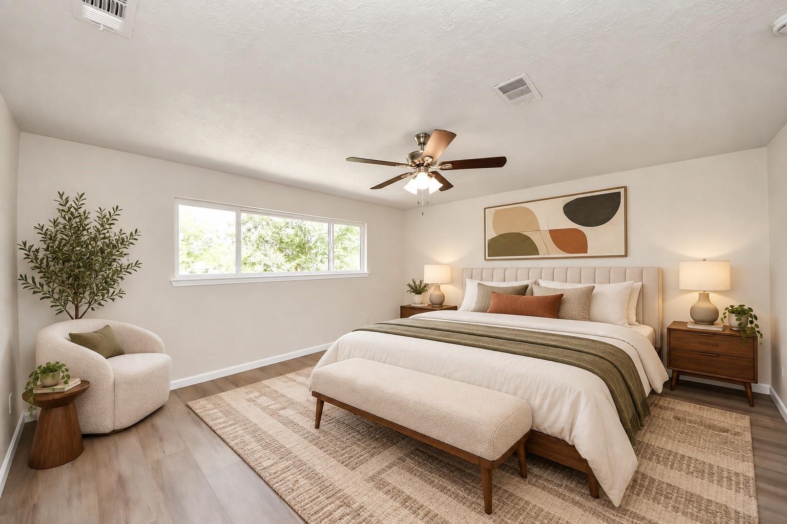 Staged bedroom with a wide window, upholstered bed, foot bench, and ceiling fan.