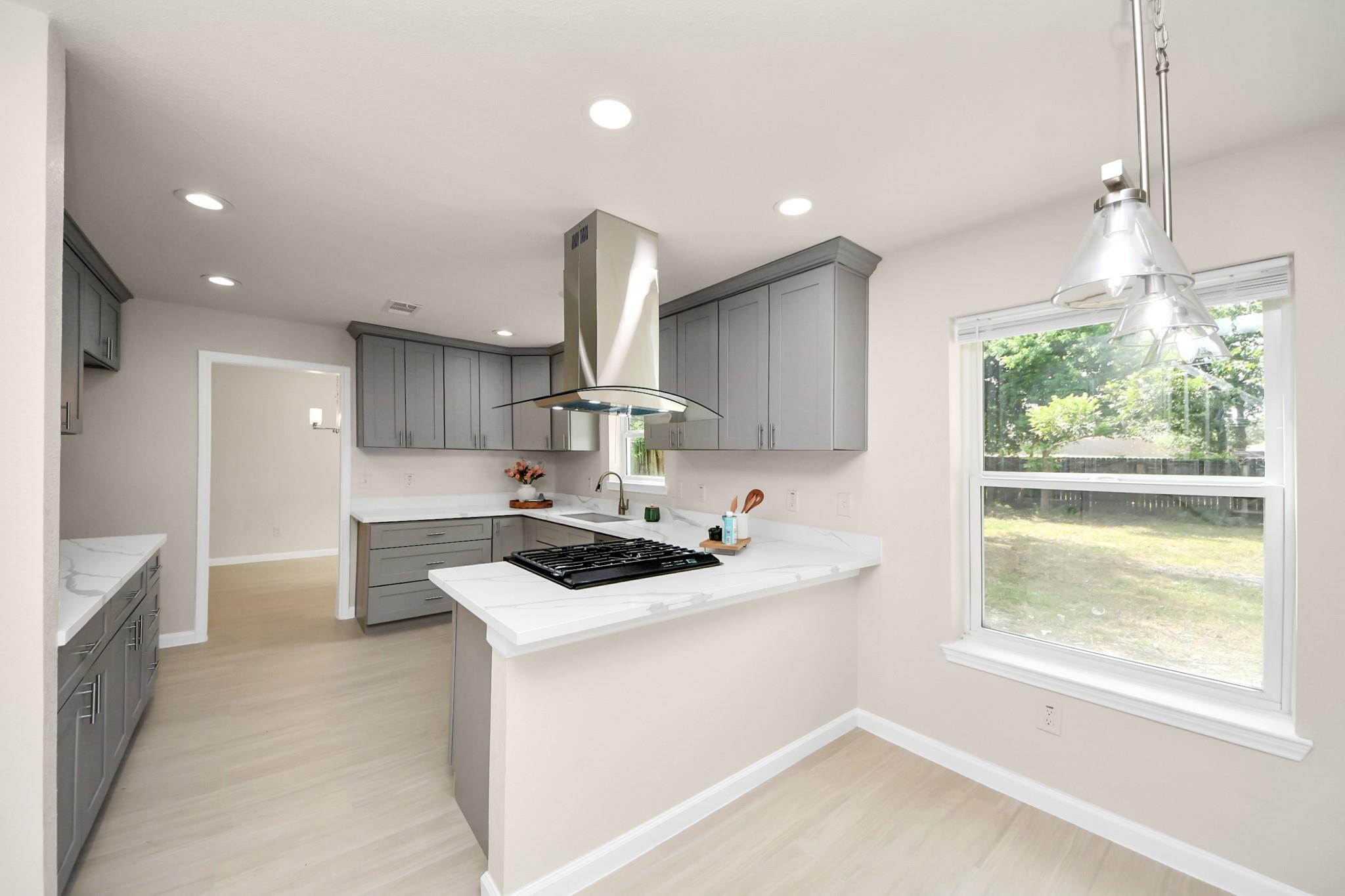 Kitchen with gray cabinets, white counters, a peninsula cooktop, and a large window overlooking the yard.