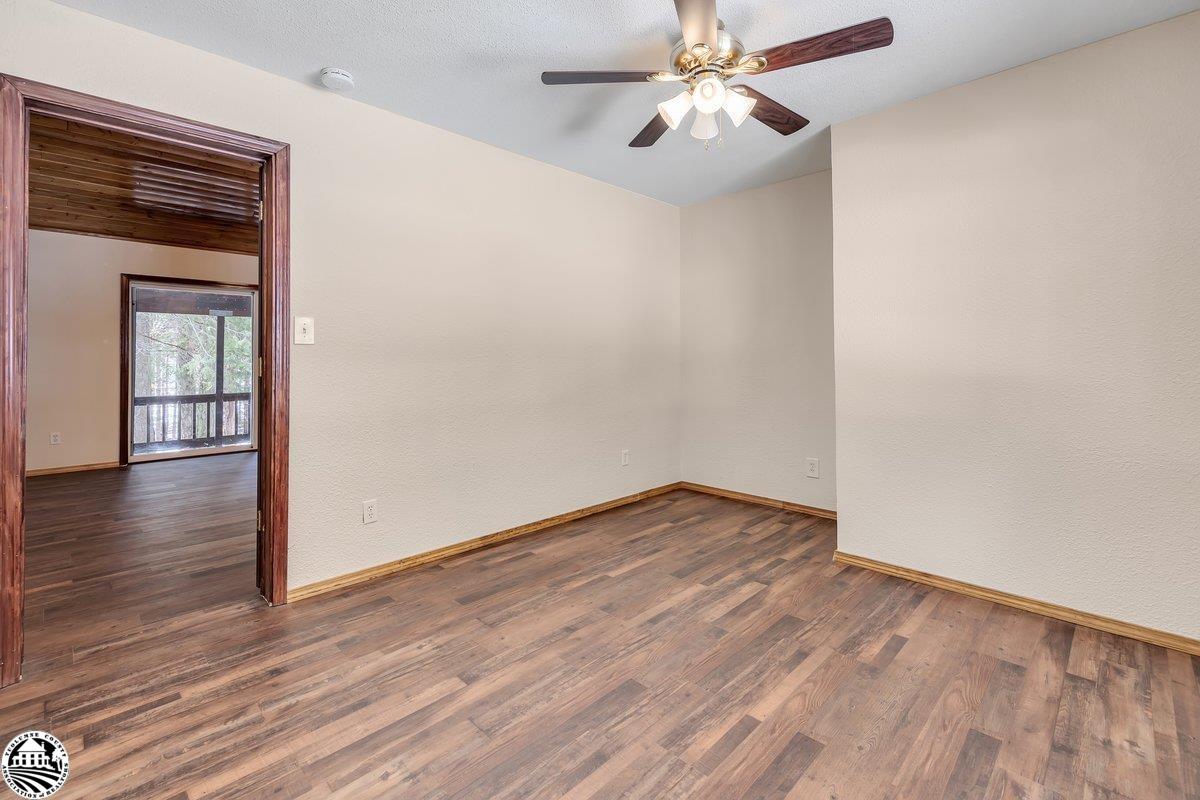 Empty room with wood-look plank flooring, a lit ceiling fan, and a wood-trimmed doorway to an adjoining room.