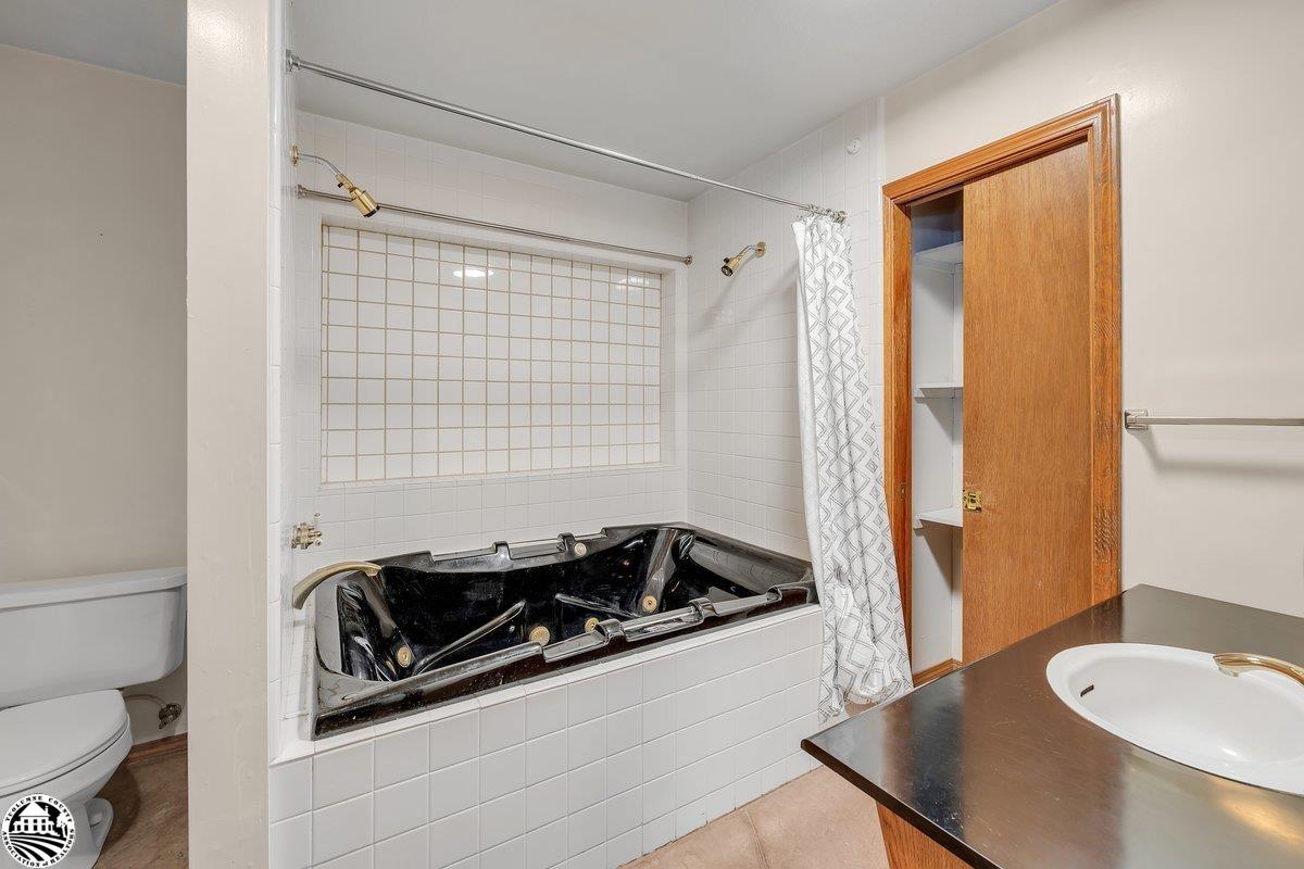 Bathroom with a black jetted tub, white tile, and a partially open wooden closet door.