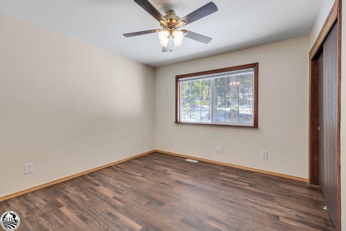Empty bedroom with dark wood-look flooring, a ceiling fan, and a window overlooking trees.
