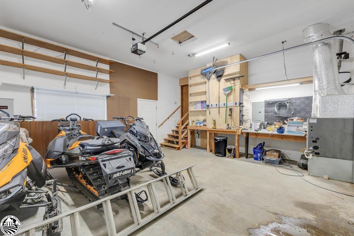 Garage workshop with snowmobiles, overhead shelves, a workbench, and large ventilation ducts.