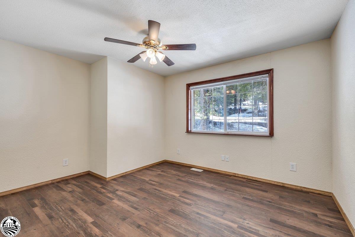 Empty room with dark wood-look flooring, a large window, and a ceiling fan with lights.