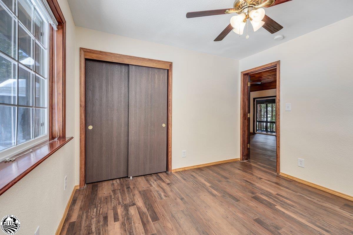 Empty bedroom with dark wood flooring, sliding closet doors, and a ceiling fan.