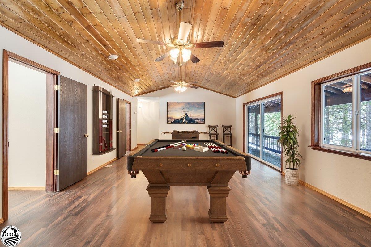 Billiard room with a pool table beneath a vaulted wood ceiling and windows overlooking trees.