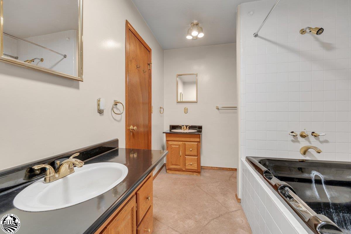 Bathroom with a long black vanity, wood cabinetry, and a black tub surrounded by white tile.