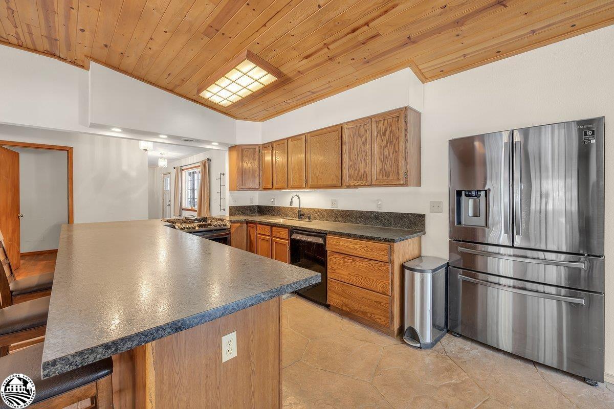 Kitchen with a large island, oak cabinetry, stainless steel appliances, and a vaulted wood ceiling.