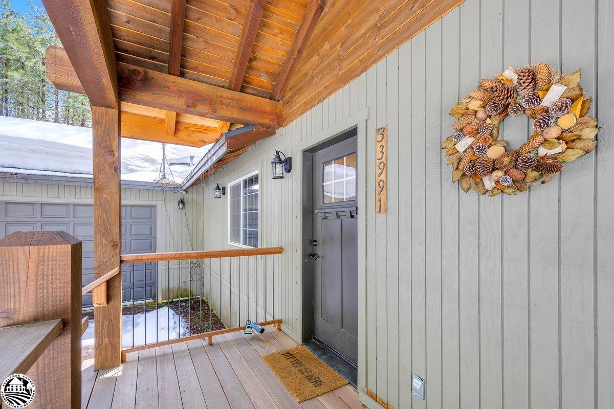 Covered front porch with a dark entry door, wooden beams, and a pinecone wreath.