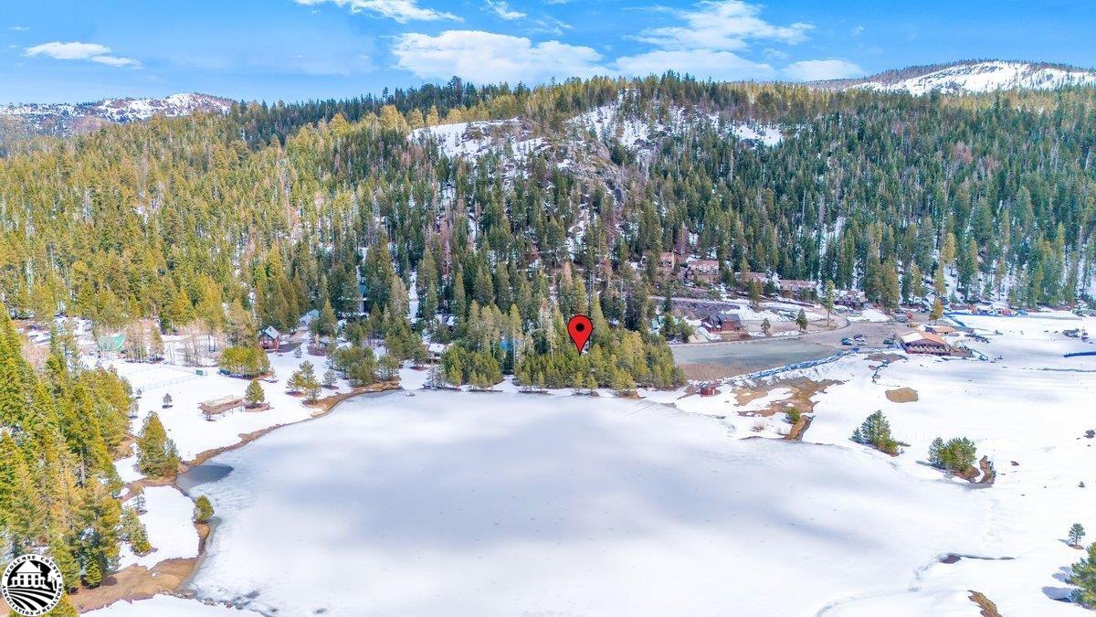 Aerial view of a frozen lake, wooded shoreline, scattered buildings, and snow-dusted hills.