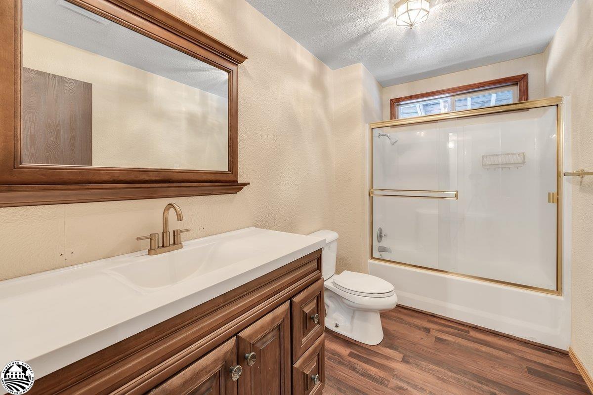 Bathroom with dark wood vanity, large framed mirror, and glass-enclosed bathtub and shower.