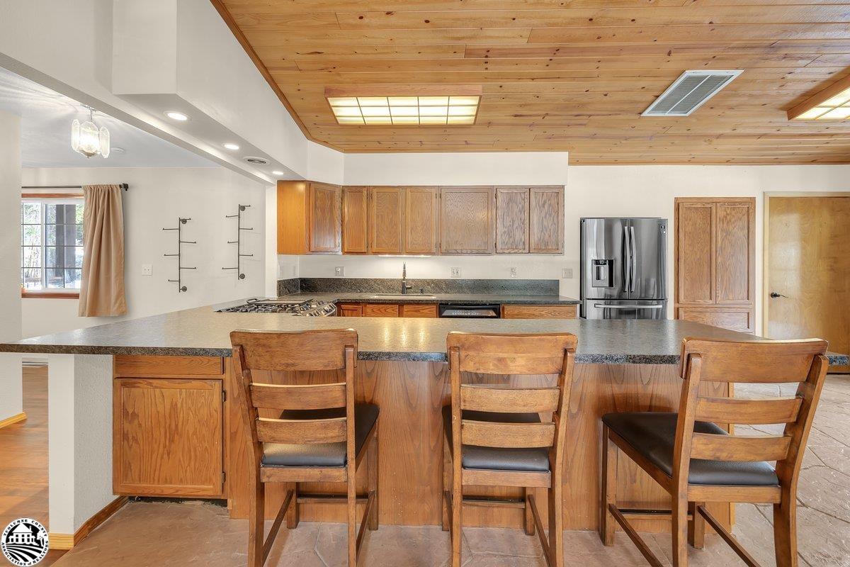 Kitchen with wood cabinetry, a broad stone island, and a pine-plank ceiling.