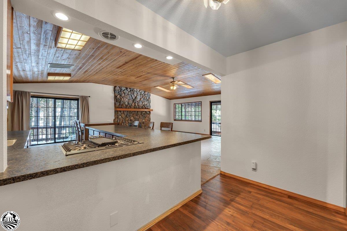 Kitchen with a gas cooktop peninsula, wood-plank ceiling, and stone fireplace in the adjoining room.