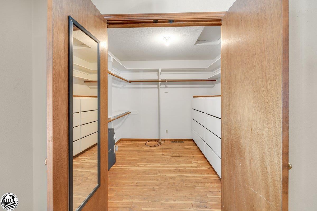 Walk-in closet with hardwood floors, white built-in drawers, wraparound hanging rods, and a full-length mirror.