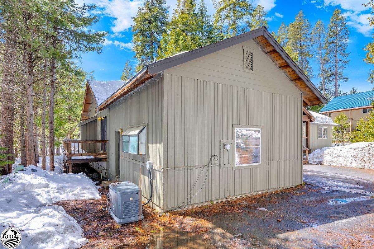 Gray-sided home among pine trees, with snow on the ground and a small side deck.