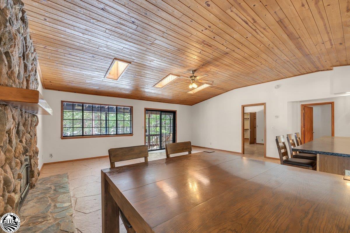 Dining area with a large wooden table, stone fireplace, and wood-plank ceiling with skylights.