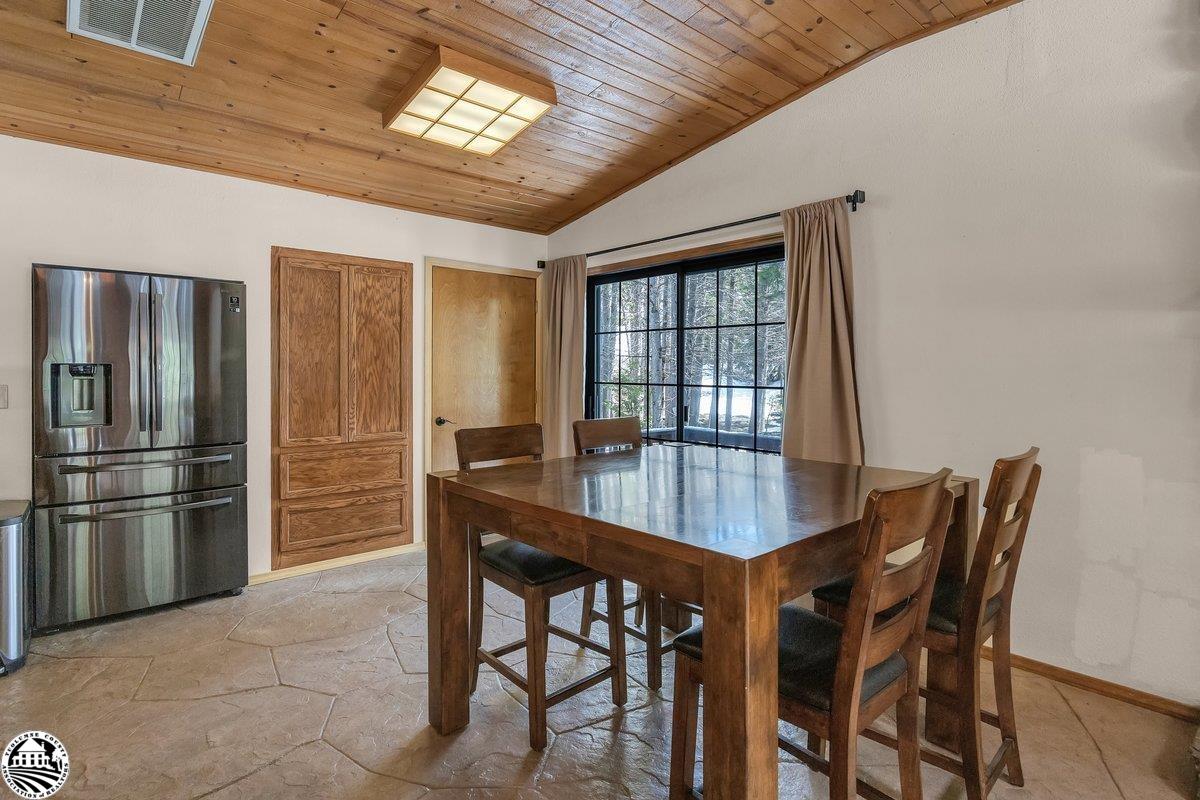 Dining area with a wooden table, stainless-steel refrigerator, and snowy trees visible through the window.