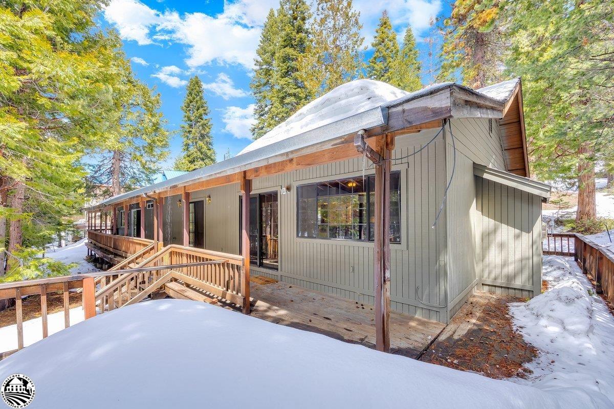 Wood-sided cabin with a raised deck, surrounded by snow and evergreen trees.