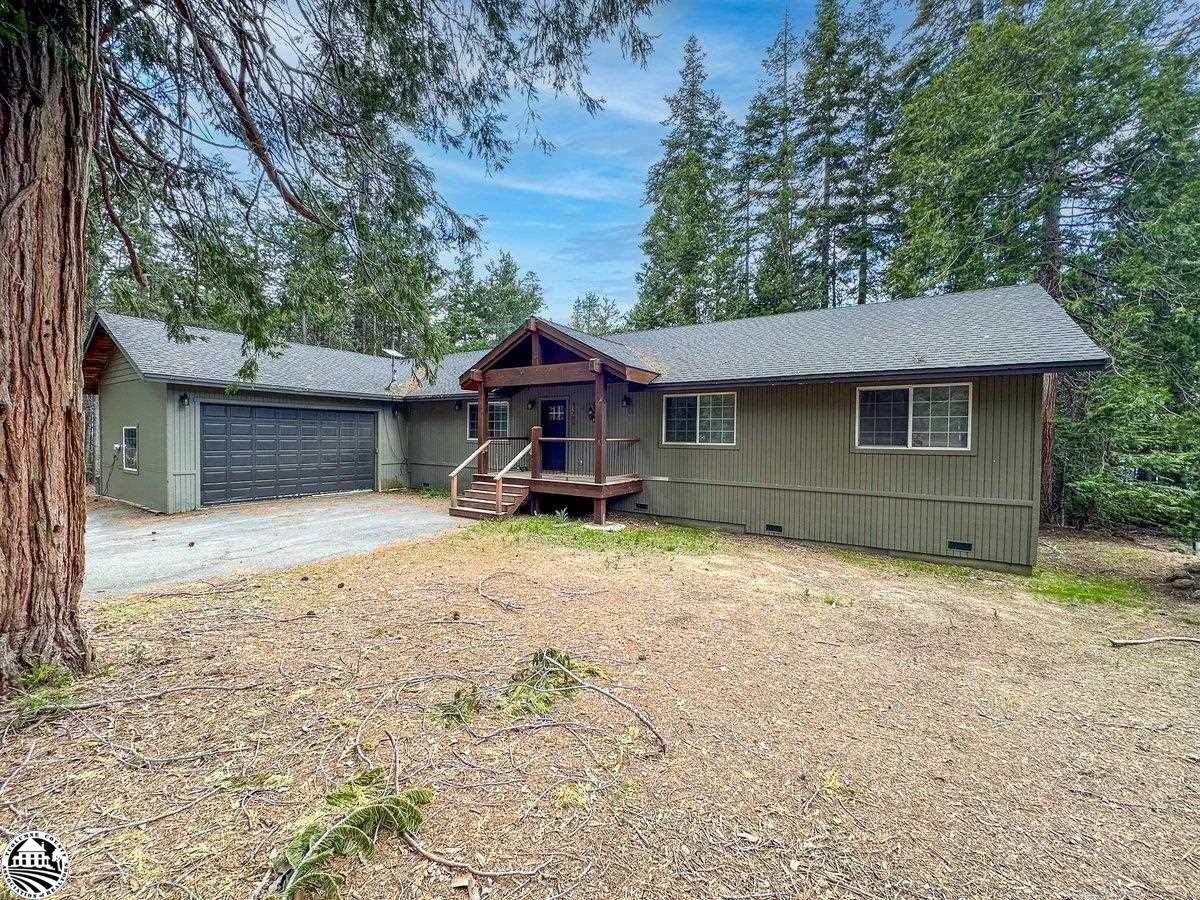 Olive-green single-story home with a double garage and covered porch among tall trees.