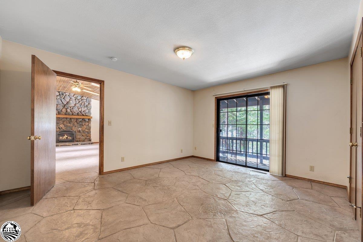 Empty room with a stone-look floor and sliding glass door beside an open doorway to a stone fireplace.