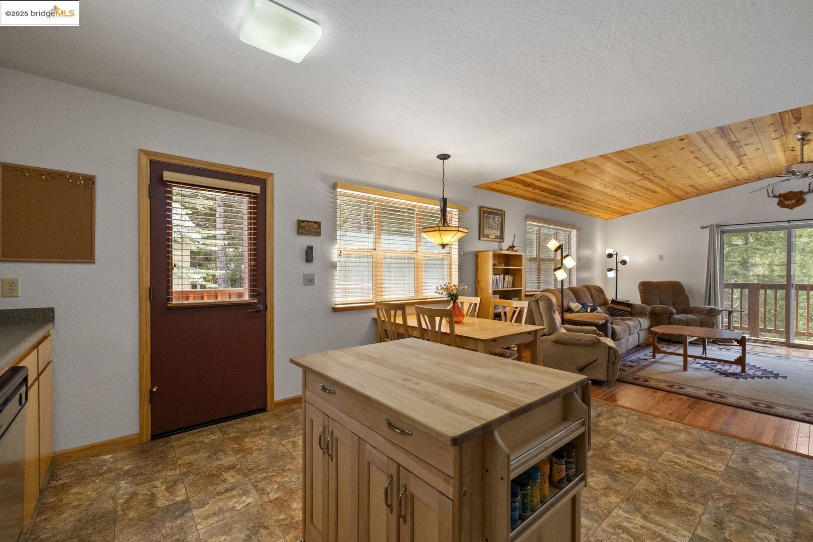 Open-plan kitchen and living room with a central wood island and vaulted wood ceiling.