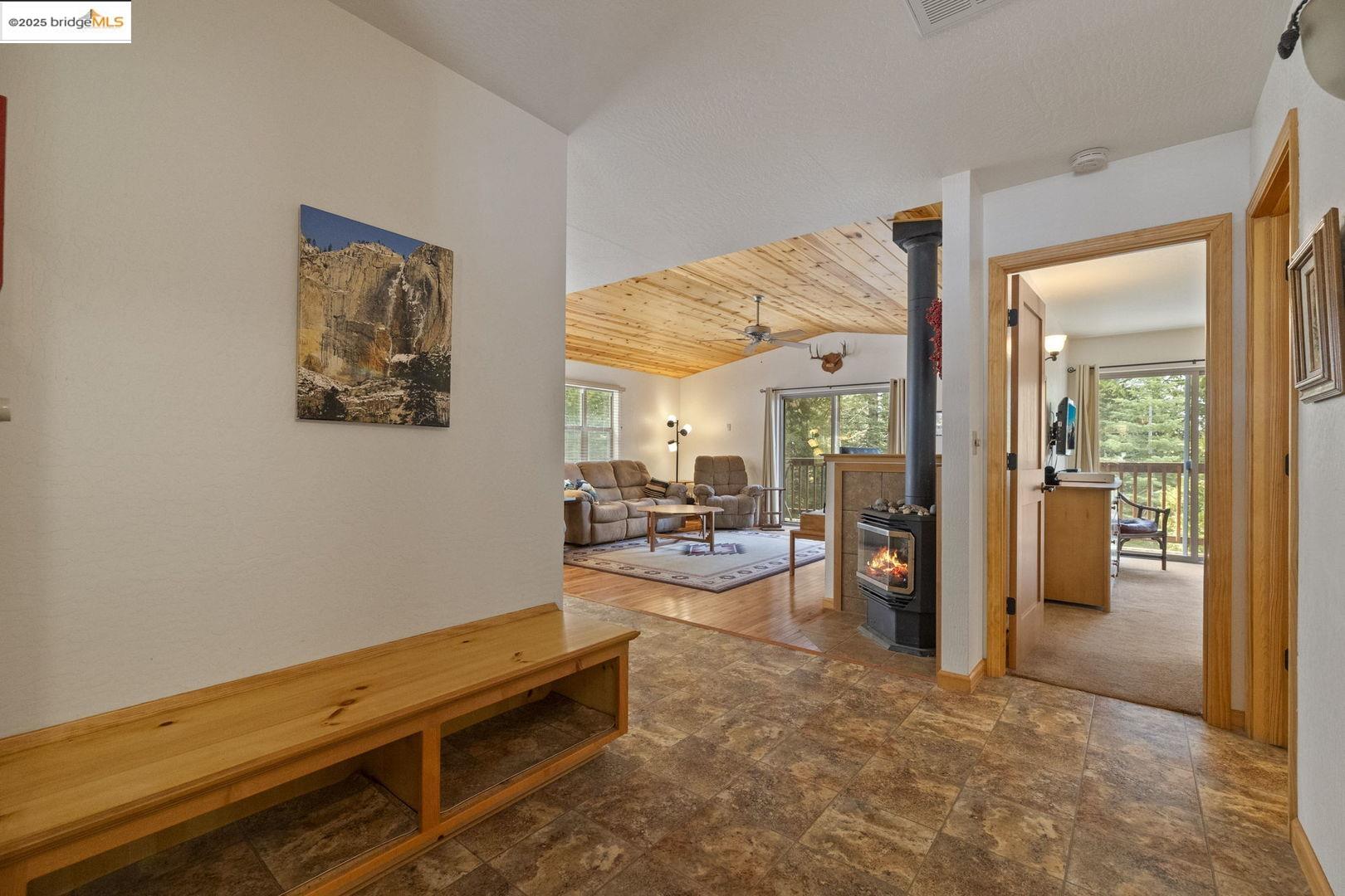 Entryway opening to a furnished living room with a wood-plank ceiling and wood-burning stove.