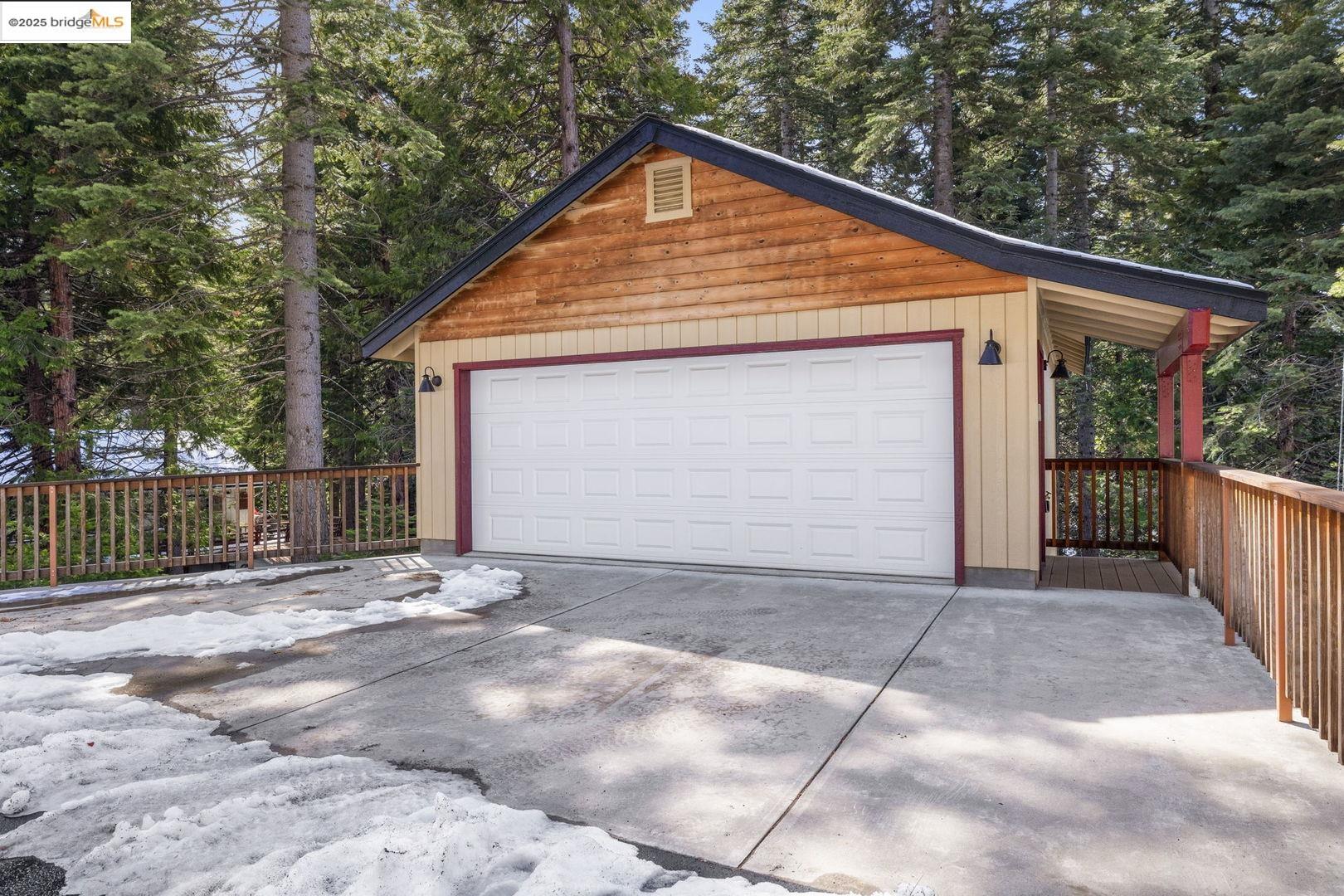 Detached garage with a wide white door, red trim, and snow on the driveway.