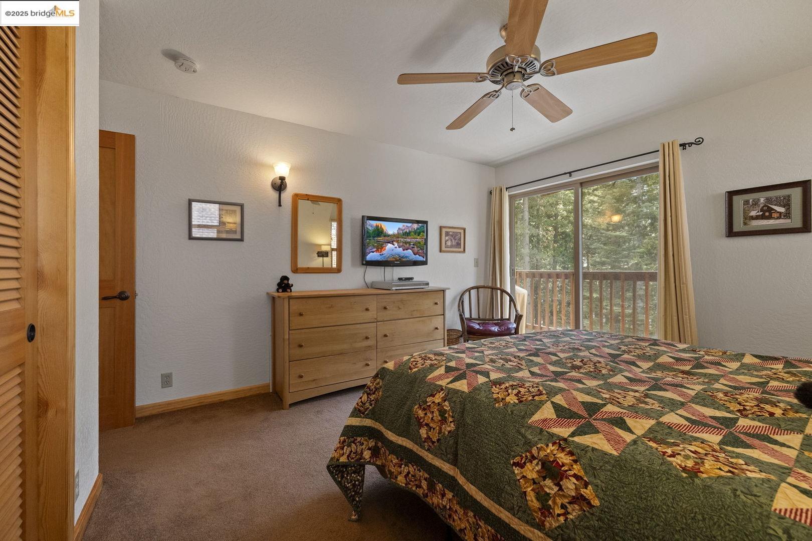Bedroom with a colorful patchwork quilt and sliding glass doors overlooking trees.