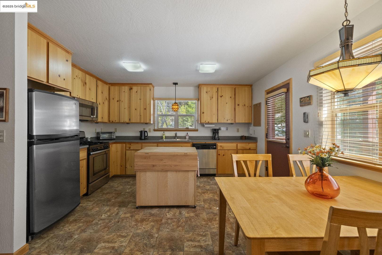 Kitchen with honey-colored wood cabinets, a butcher-block island, and an adjoining dining table by large windows.