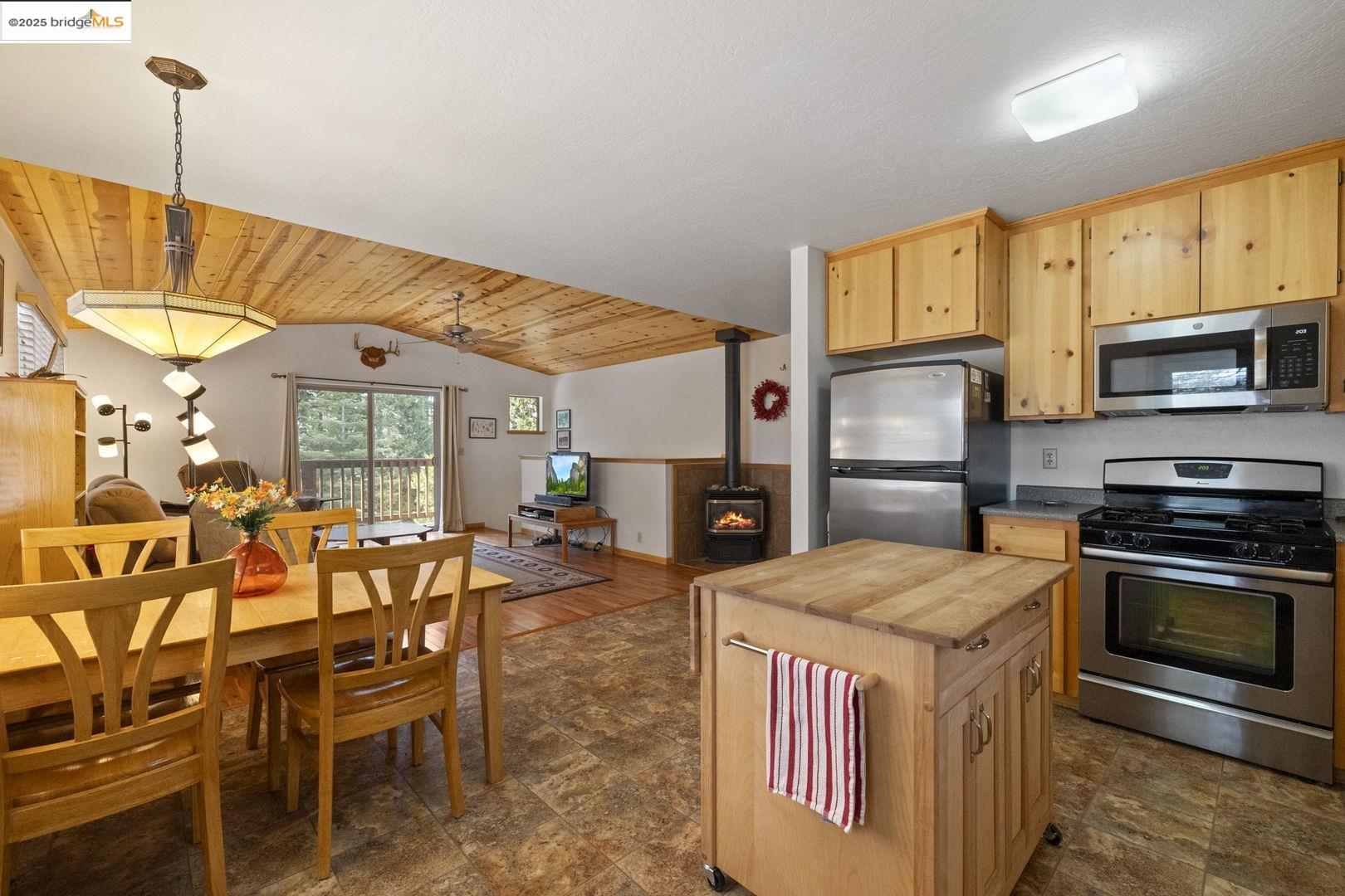 Open-plan kitchen and dining area with a wood-plank ceiling, central island, and stainless steel appliances.