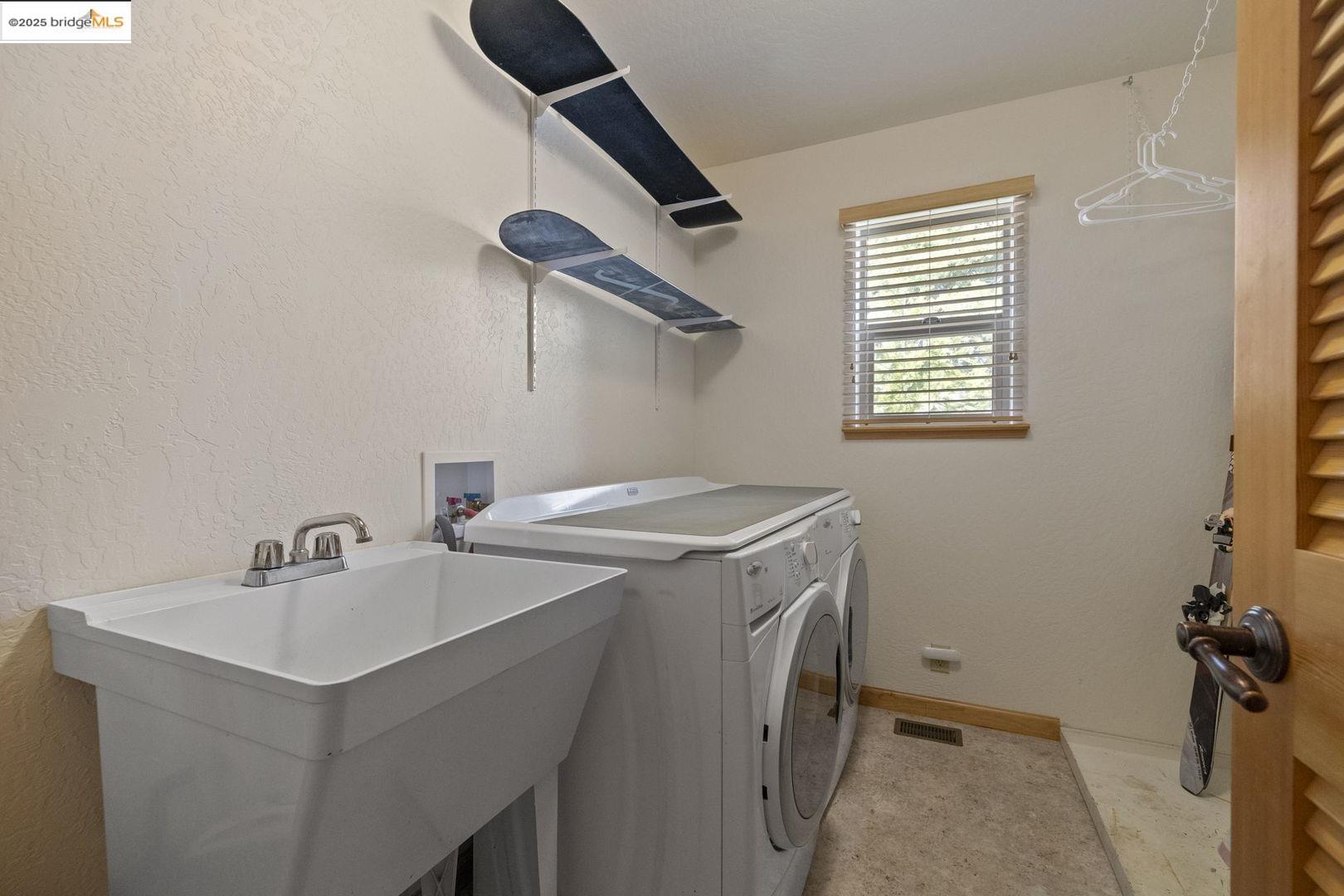 Laundry room with a utility sink, washer and dryer, and snowboards on wall shelves.