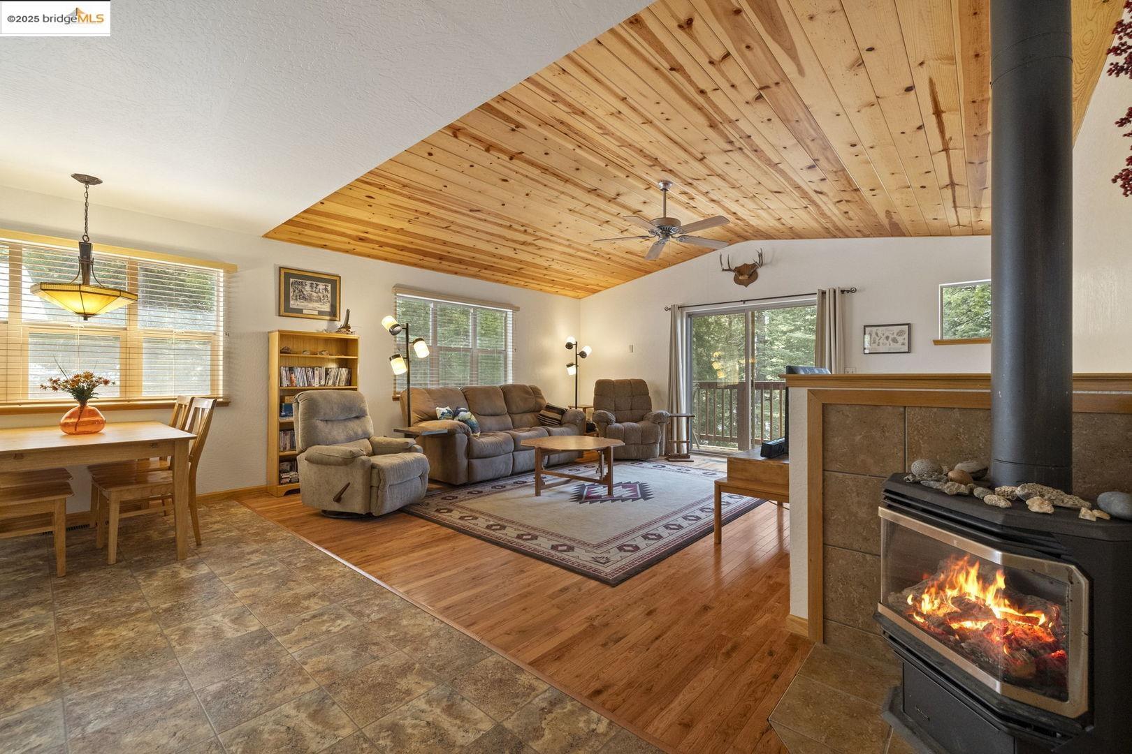 Living room with vaulted wood ceiling, hardwood floors, and a lit wood-burning stove.