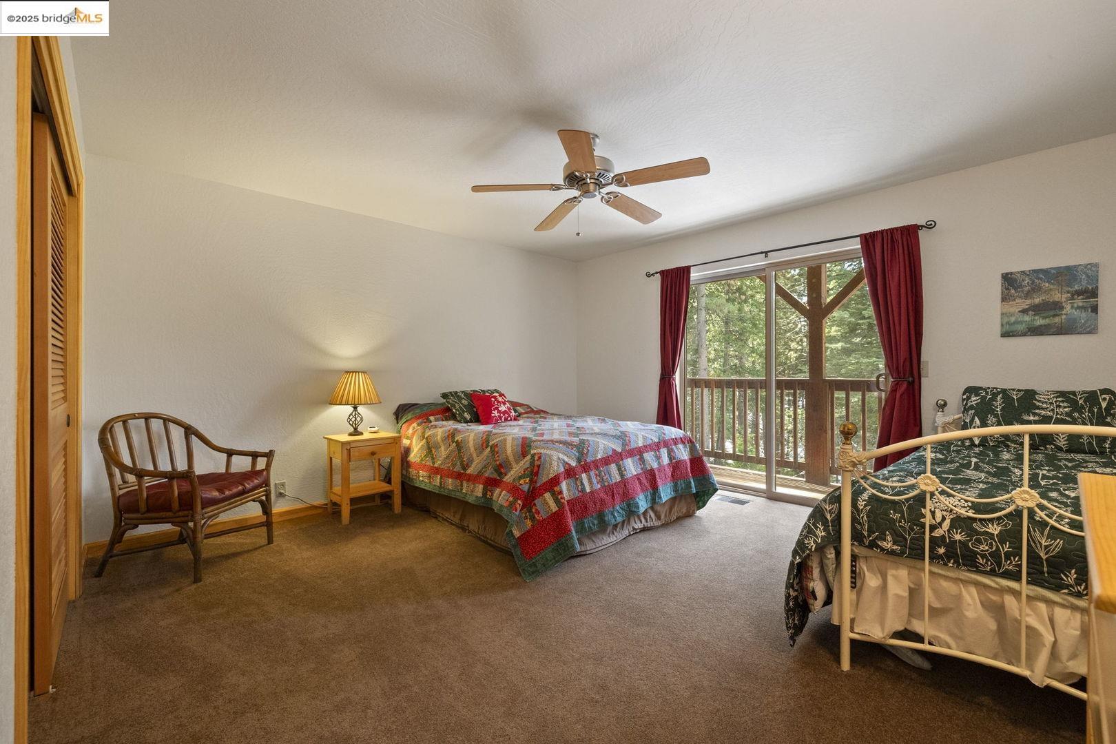 Bedroom with two beds, a ceiling fan, and sliding glass doors overlooking trees.
