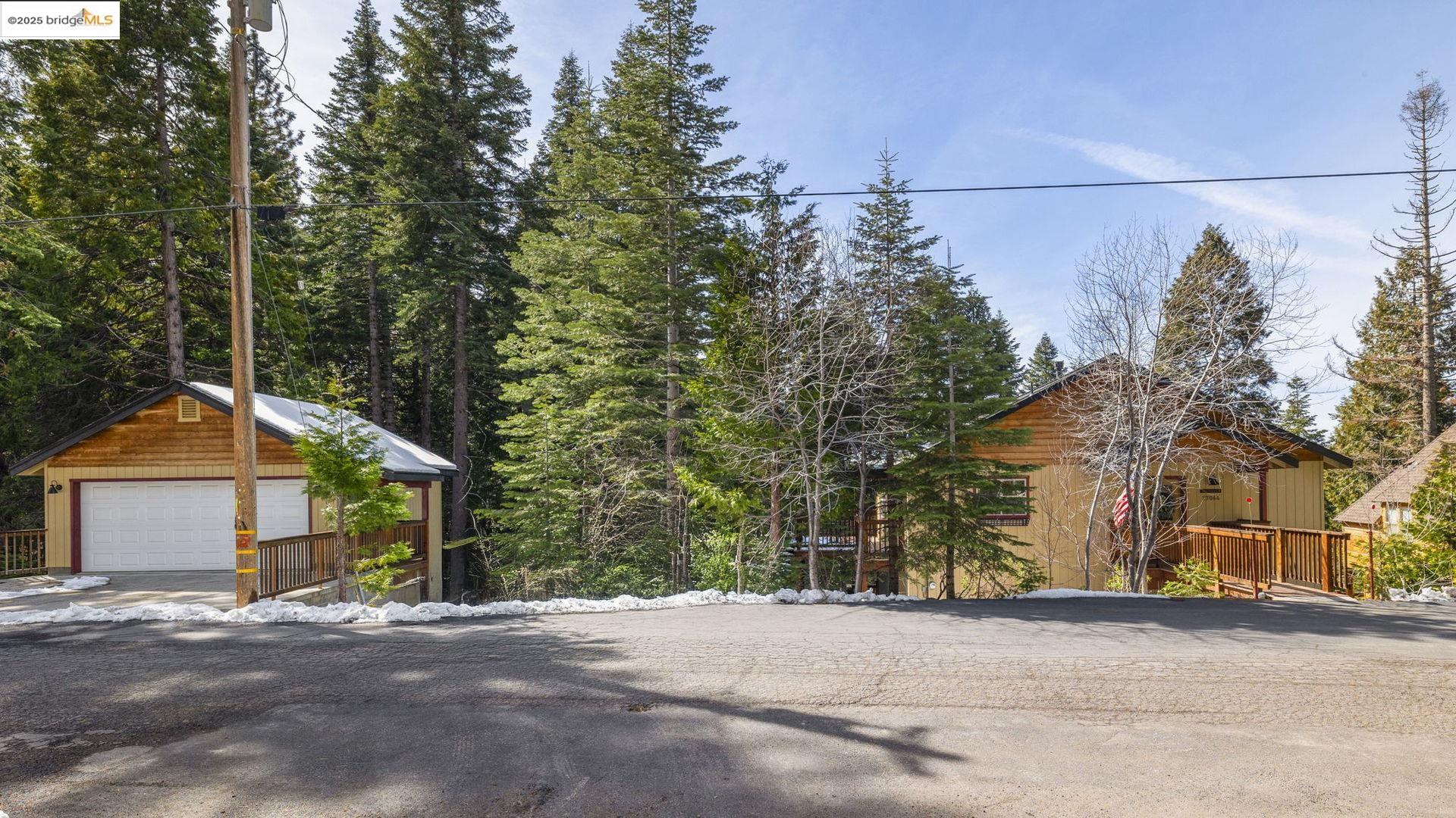 Wood-sided mountain home with a front deck and detached garage among evergreen trees.