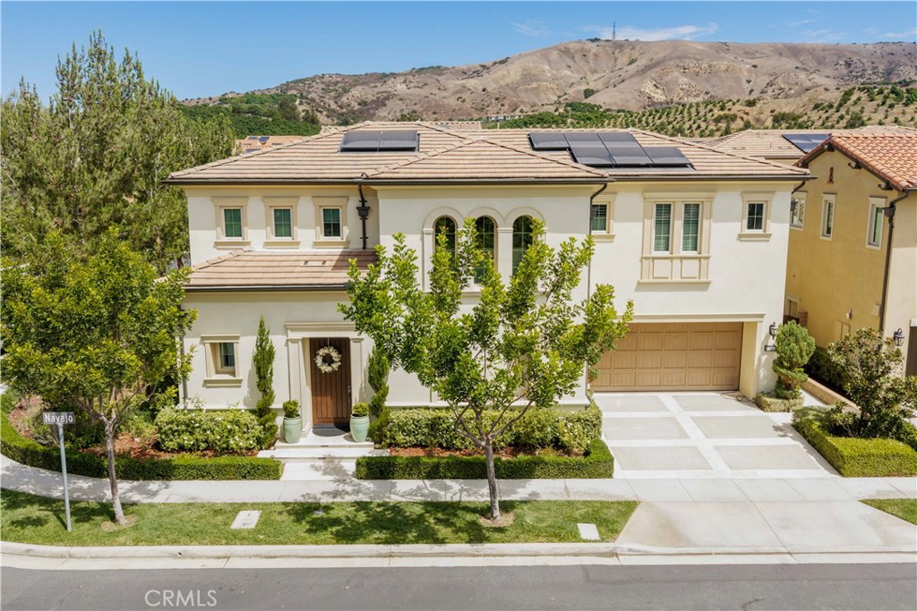 Two-story stucco home with solar panels, tiled roof, and landscaped front yard.