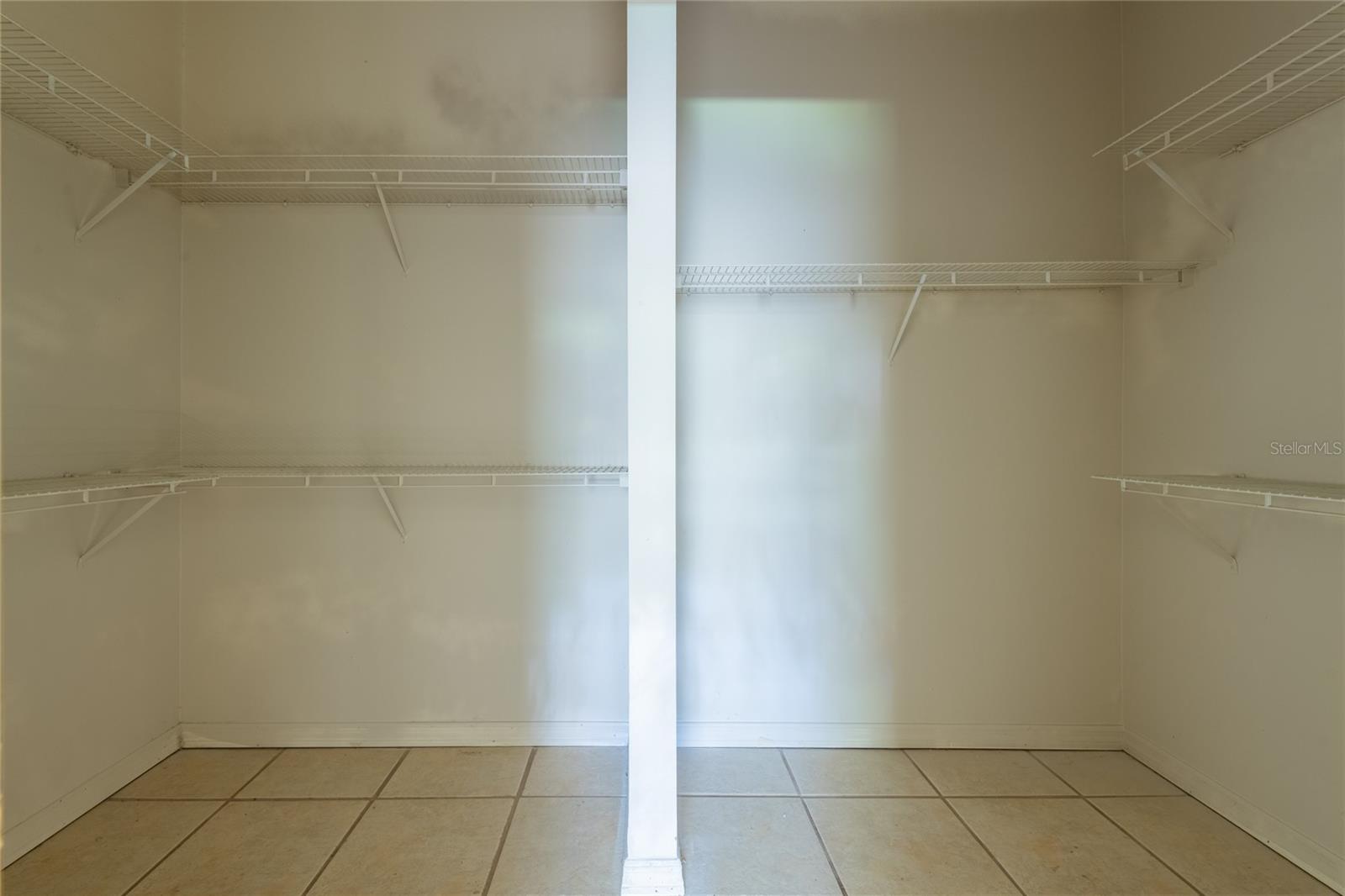 Empty walk-in closet with white wire shelves and beige tile flooring.