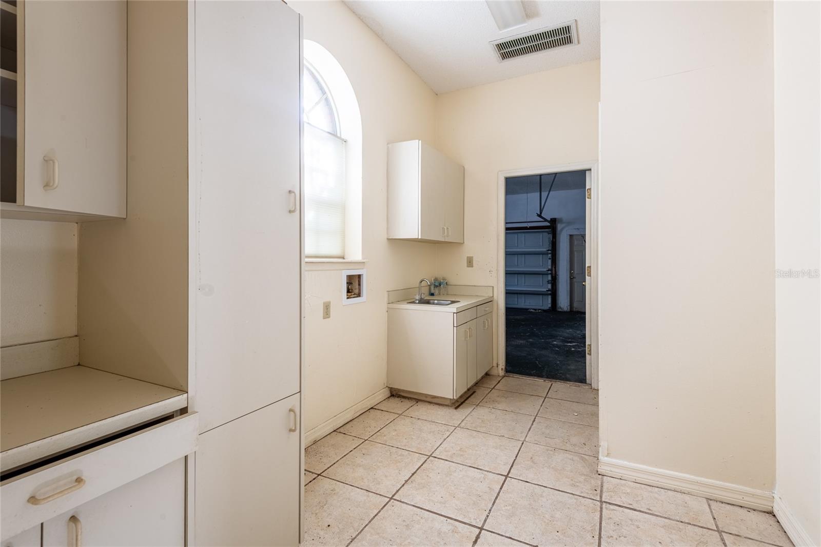 Laundry room with white cabinets, a utility sink, tiled floor, and a doorway to the garage.