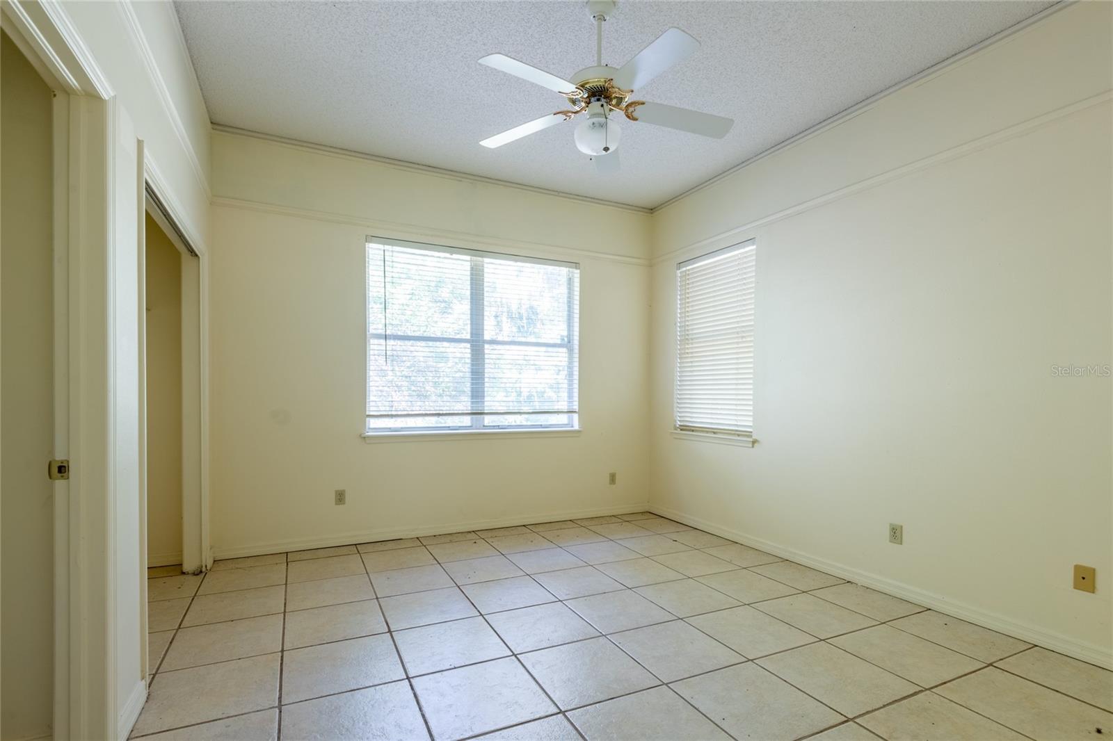 Empty tiled room with two windows and a ceiling fan.