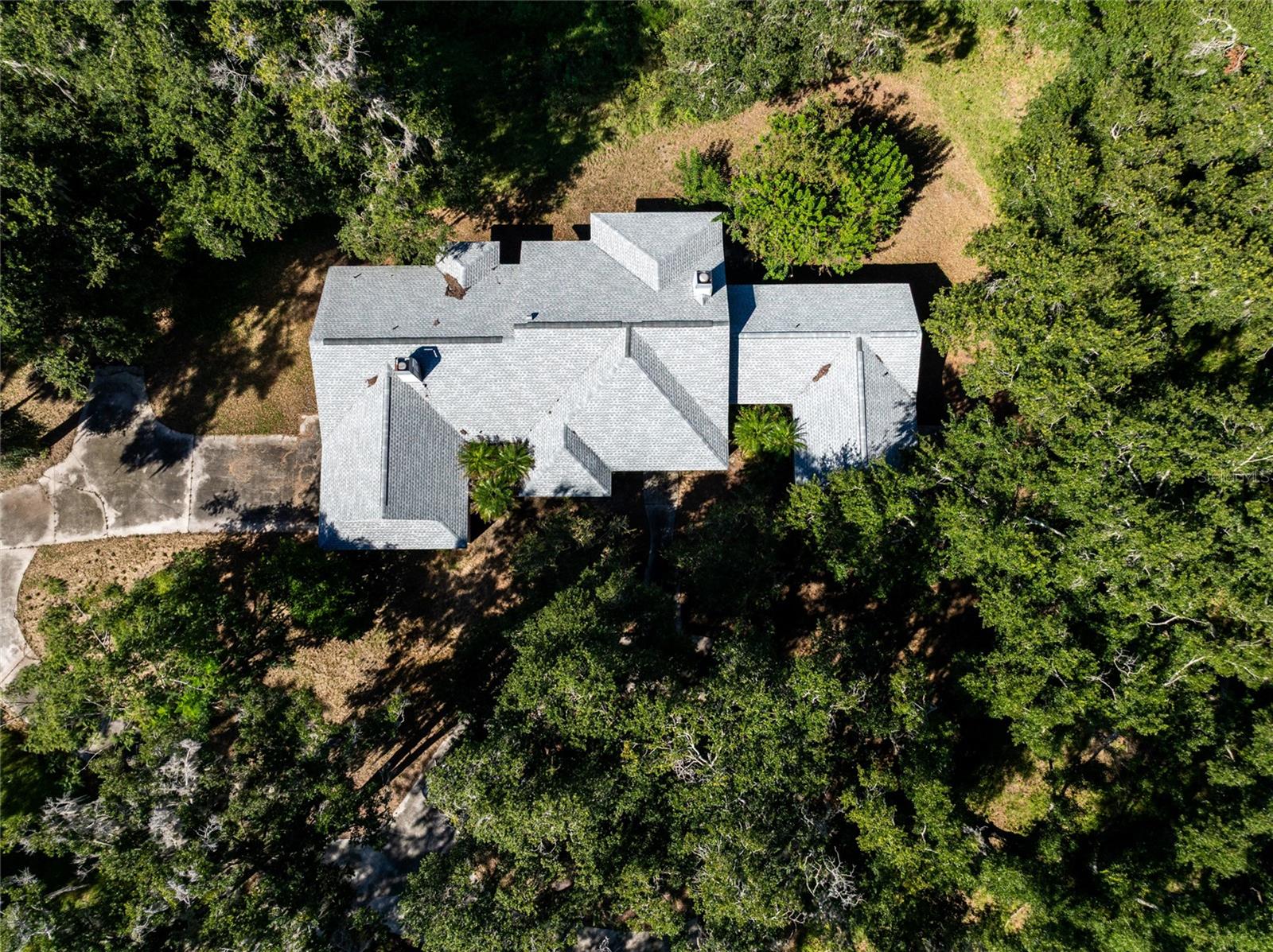 Aerial view of a gray-roofed home surrounded by mature trees, with a paved driveway.