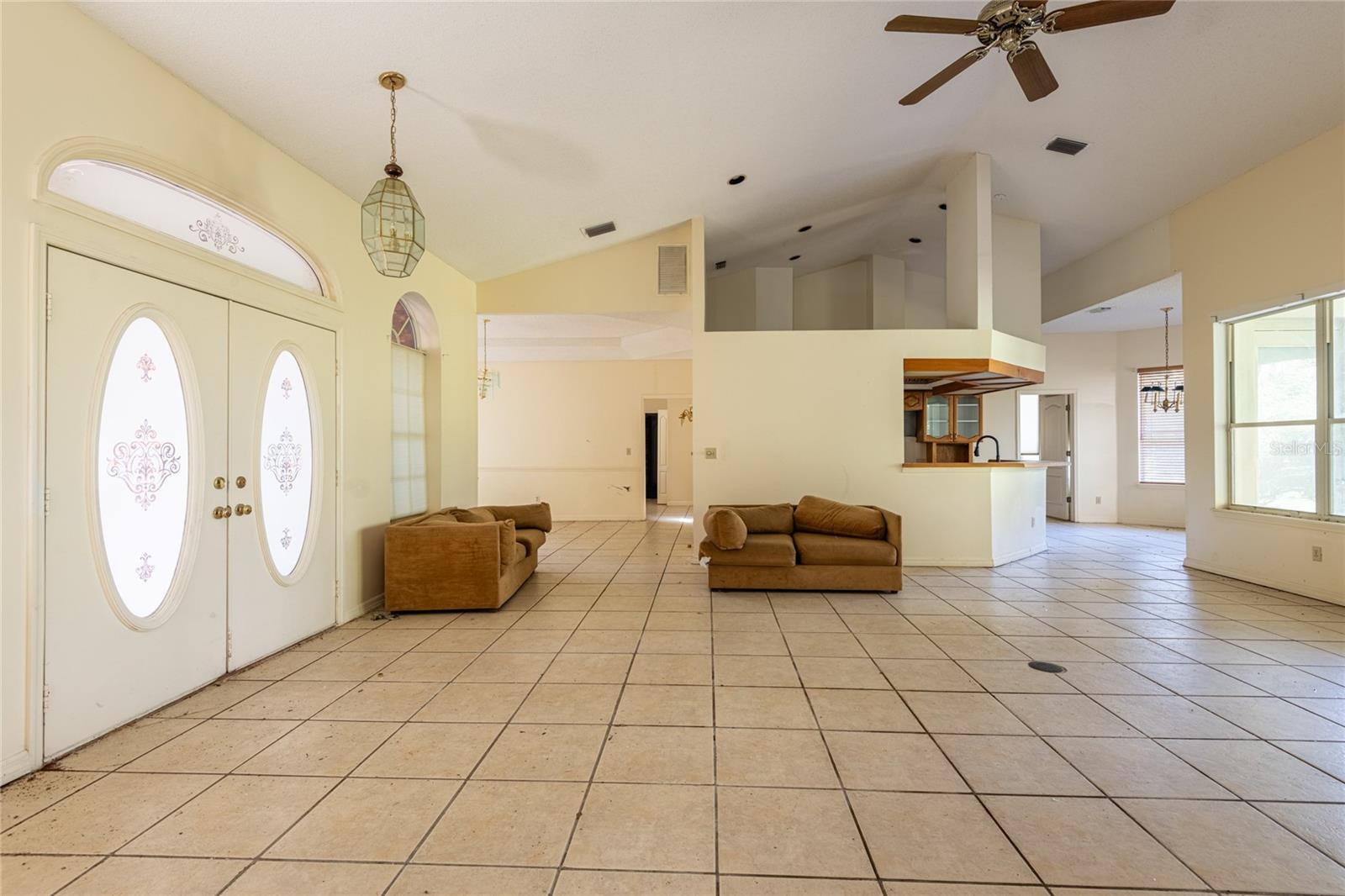 Open living area with cream tile floors, brown sofas, and ornate double entry doors.