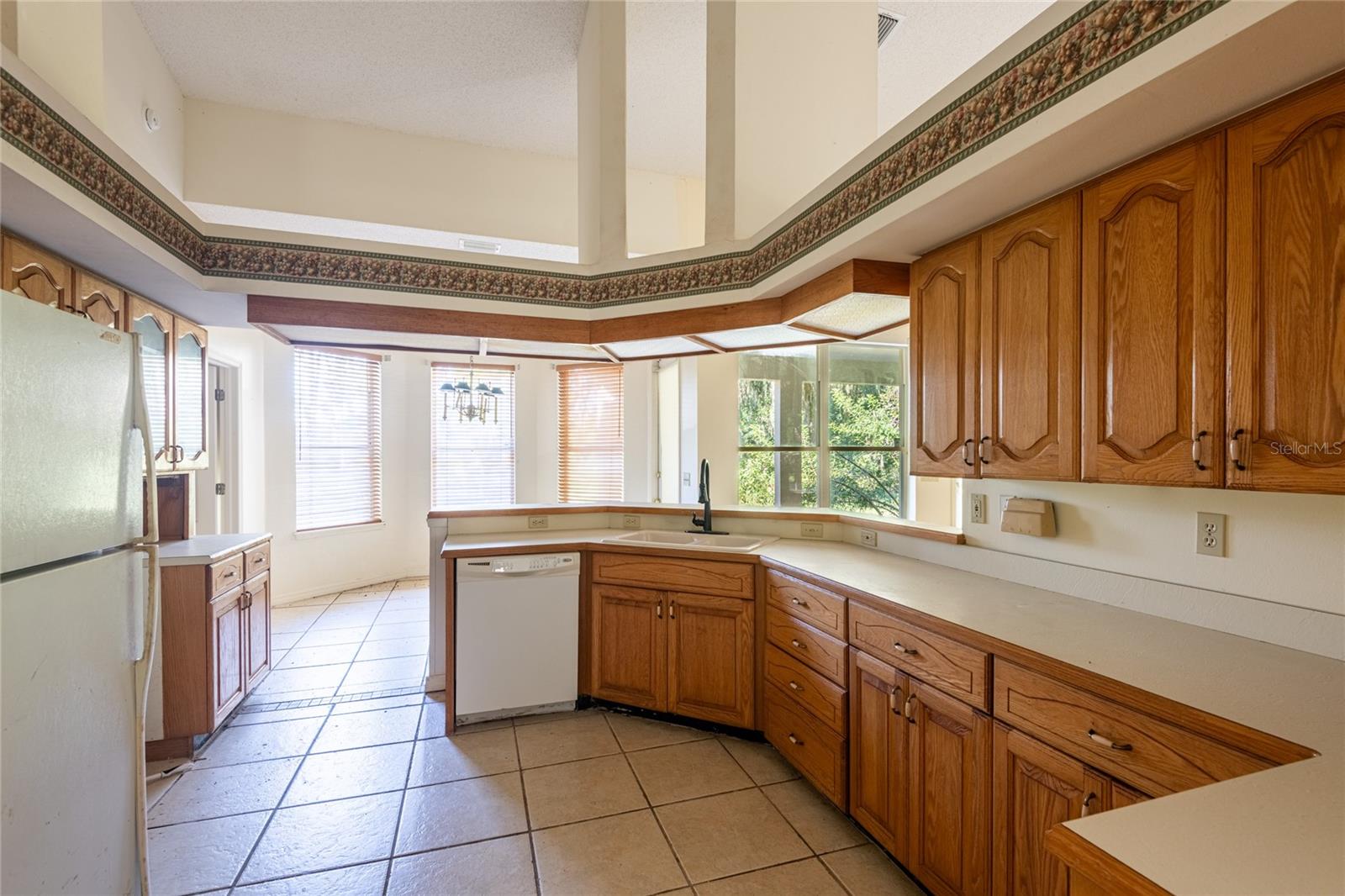Kitchen with honey-oak cabinetry, a sink peninsula, white appliances, and a tiled floor.