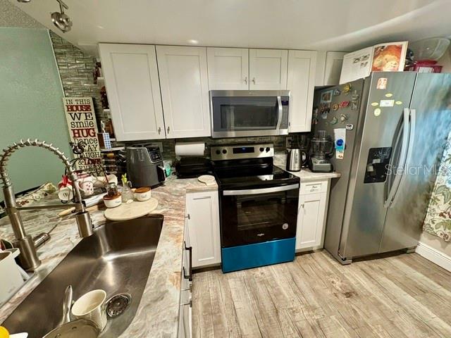 Kitchen with white cabinets, stainless refrigerator, black range, and double-basin sink.