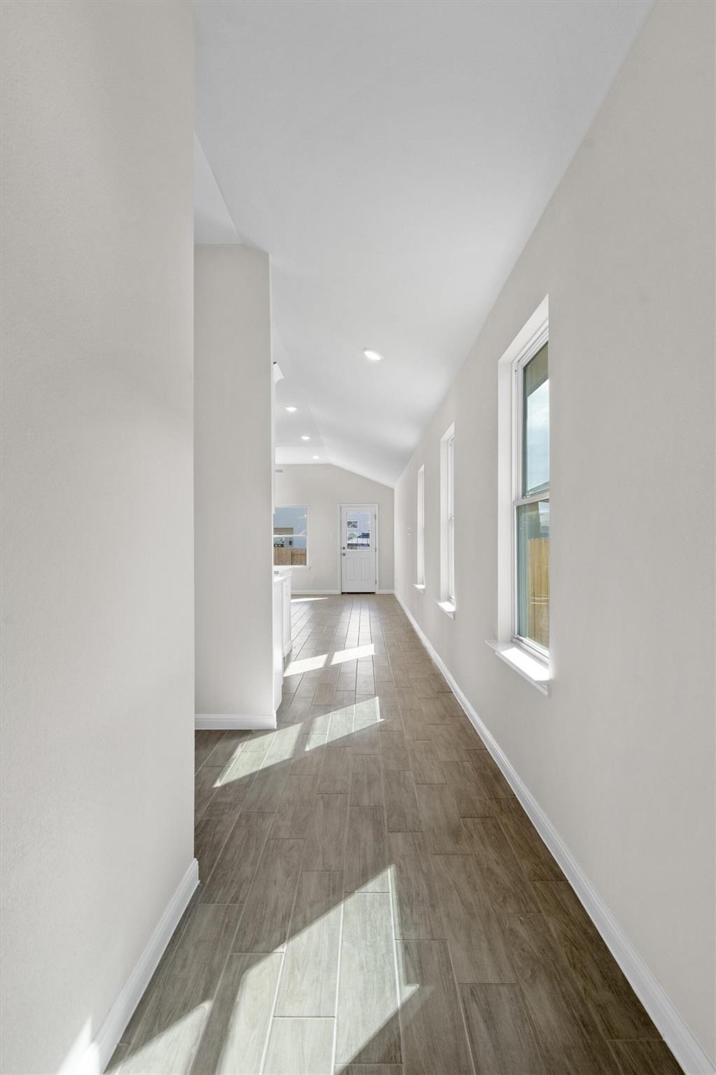 Vacant hallway with tile floors, tall windows, and sunlight streaming across the floor.